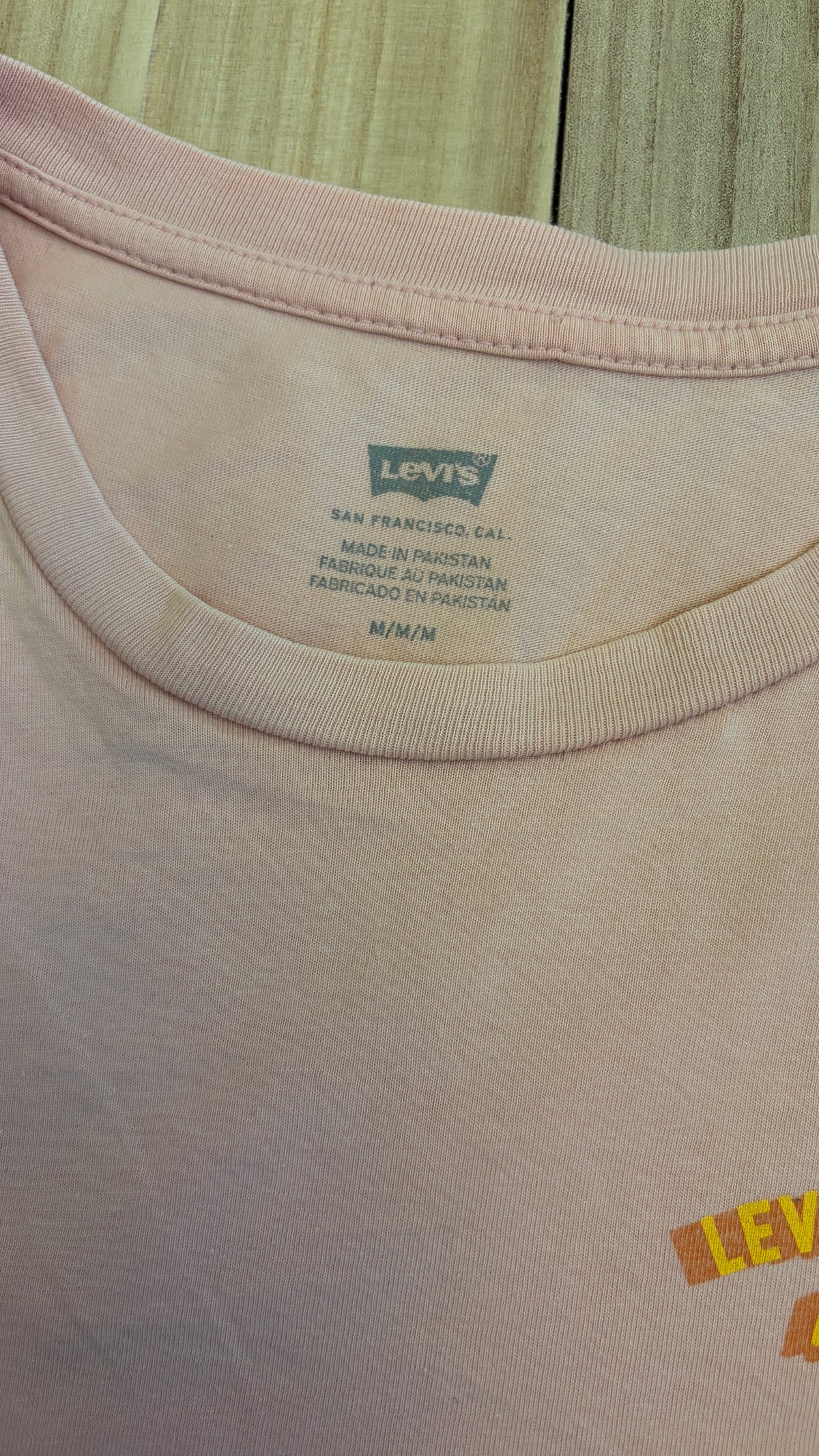Close-up view of the inner neck area of a light pink Levi's t-shirt showing the printed Levi's Batwing logo, San Francisco, Cal., Made in Pakistan, and size M