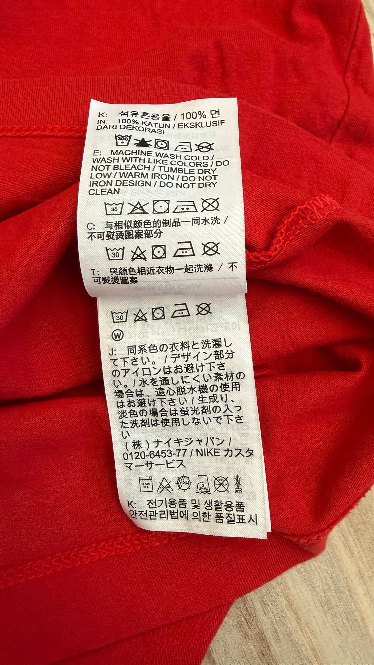 Close-up view of the inner care tag on a red Nike t-shirt displaying laundry symbols and washing instructions in English, Chinese, and Japanese with Nike Japan customer support information