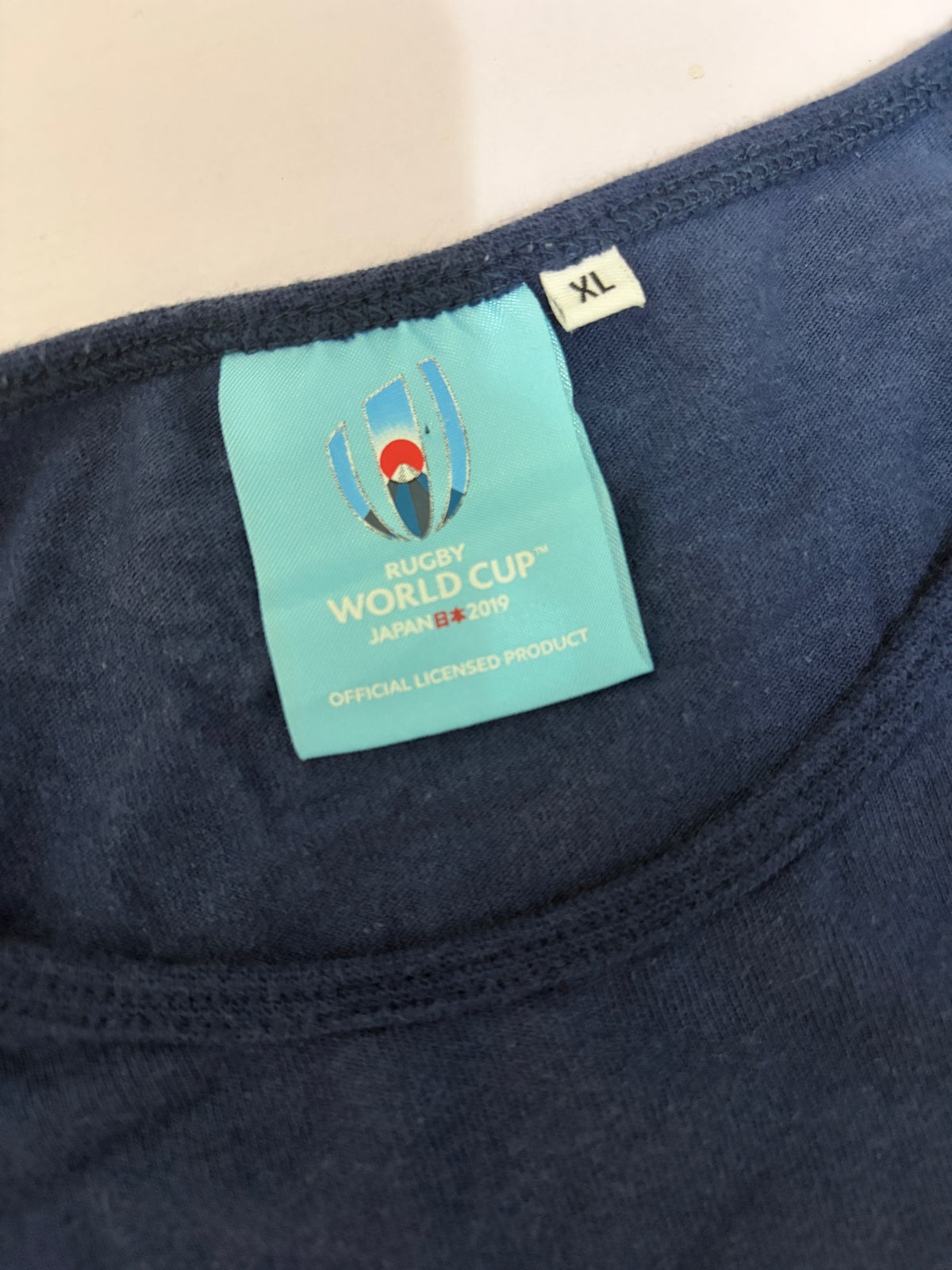 Close-up detail of the light blue Rugby World Cup Japan 2019 official licensed product neck label and size XL tag