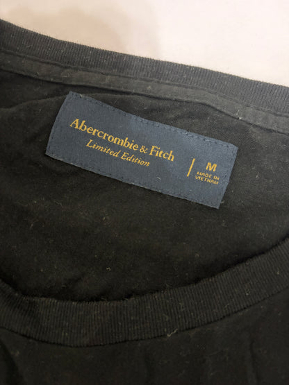Close-up detail of the navy blue Abercrombie & Fitch Limited Edition woven neck tag and size M label on a black t-shirt