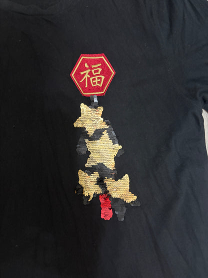Close-up detail of the embroidered red hexagonal Chinese Fu character patch and gold sequin panda embroidery on a black t-shirt