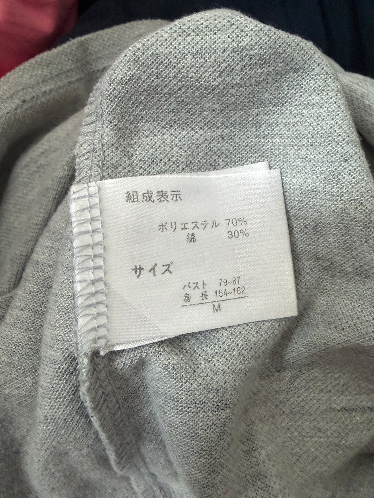 Close-up detail of the inner white care label showing size M and 70% polyester 30% cotton material composition on a heather grey polo shirt