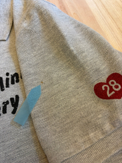 Close-up view of a grey Disney Minnie Mouse polo shirt sleeve showing a small brown stain defect pointed out by a blue sticker.