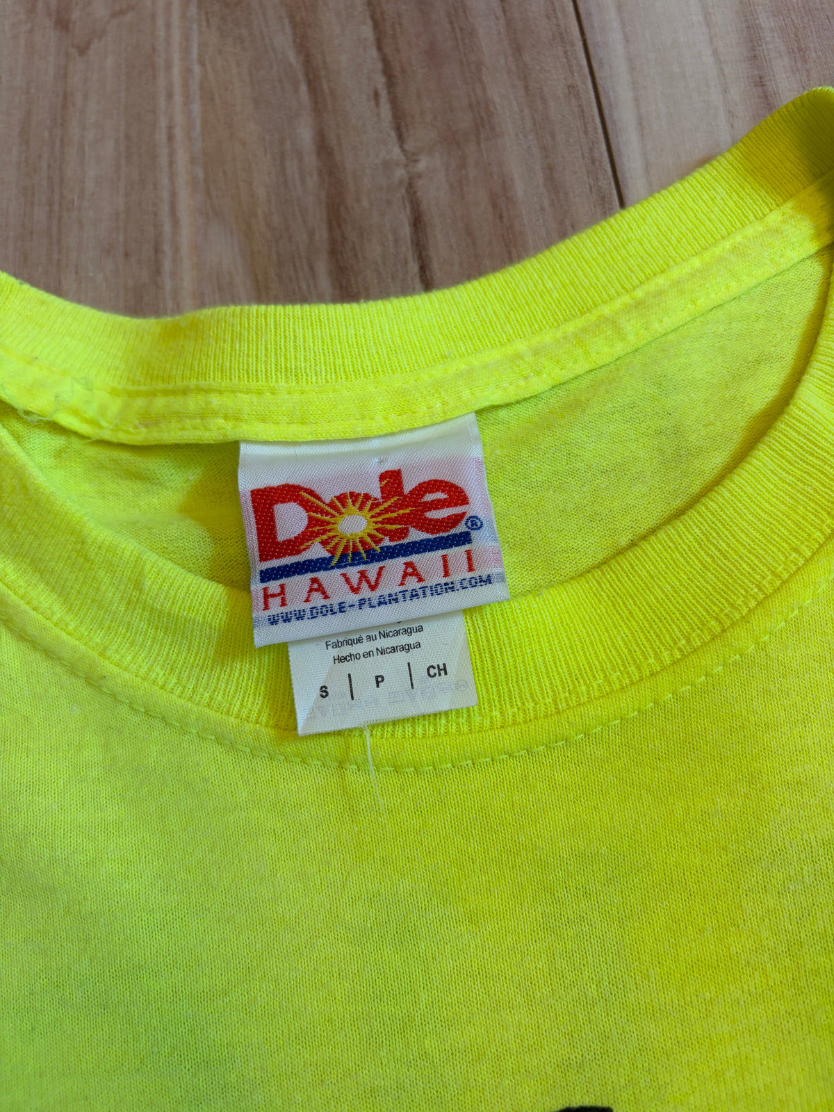 Close-up view of the inner neck tag on a neon yellow Dole Plantation Hawaii t-shirt displaying the Dole logo, website address, Made in Nicaragua, and size Small