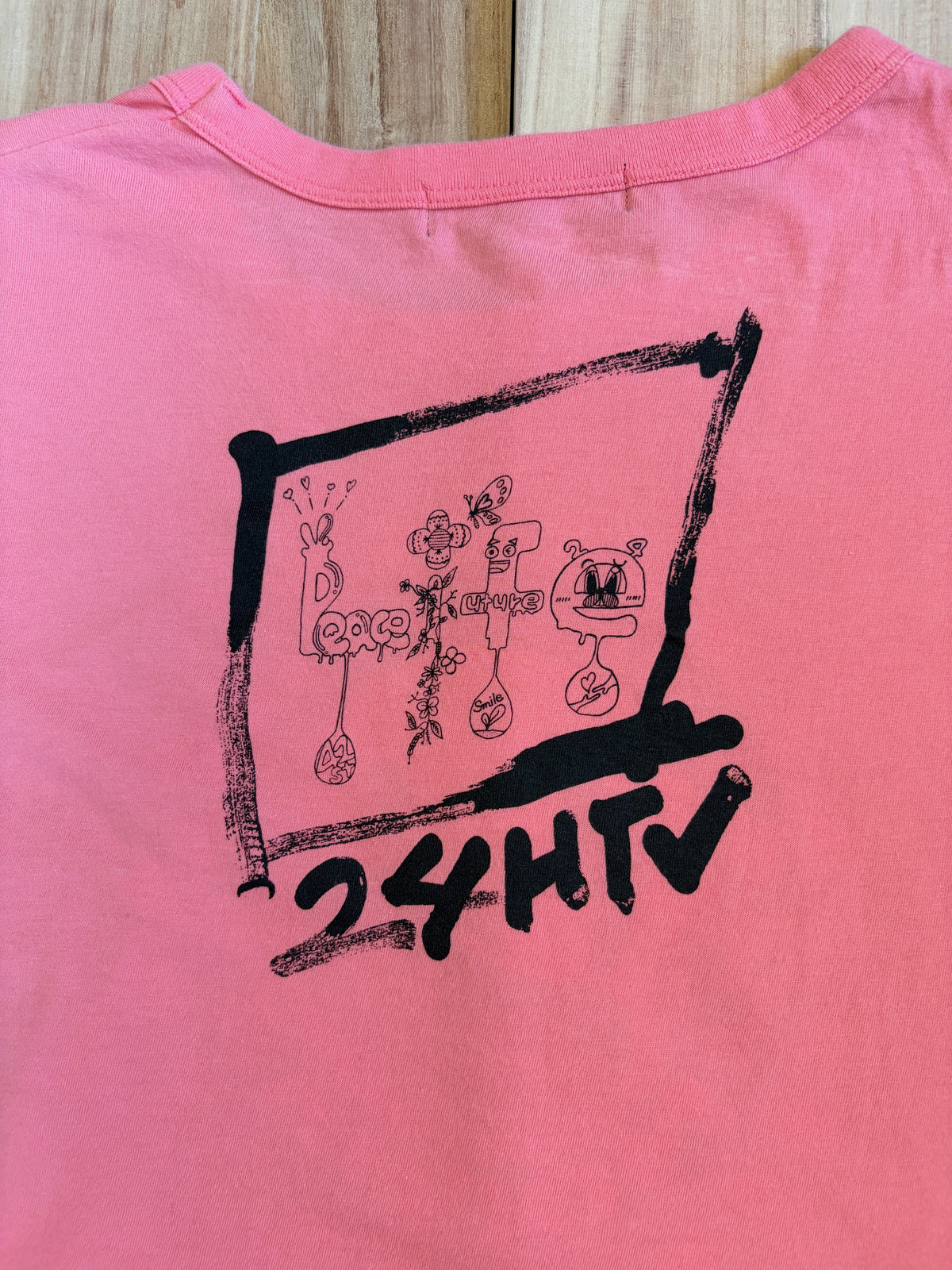 Back view of a pink Hattie Stewart x 24 Hour Television 41st charity t-shirt featuring a black frame print enclosing illustrated letters spelling LIFE and 24HTV lettering