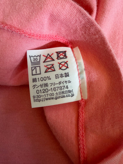 Close-up view of the inner white fabric tag on a pink t-shirt showing laundry symbols, 100% cotton material composition, Made in Japan, and Gunze Limited manufacturer contact details