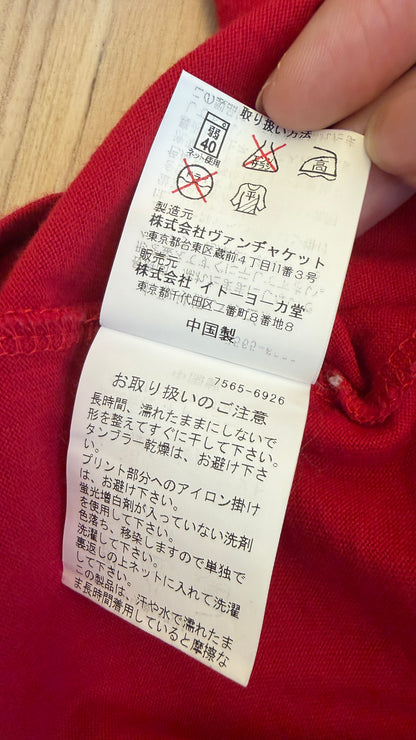 Close-up view of the inner white Japanese care instruction tag on a red t-shirt showing laundry symbols, manufacturer VAN Jacket Inc., distributor Ito-Yokado Co., Ltd., Made in China, and care notes