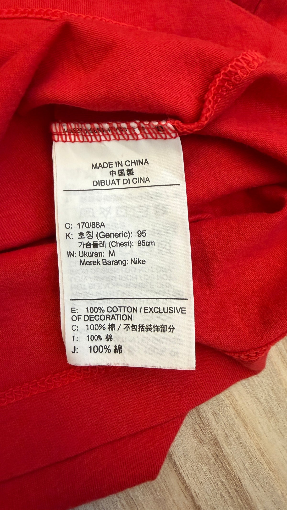 Close-up view of the white inner tag on a red Nike t-shirt indicating Made in China, size M (170/88A), and 100% cotton material composition
