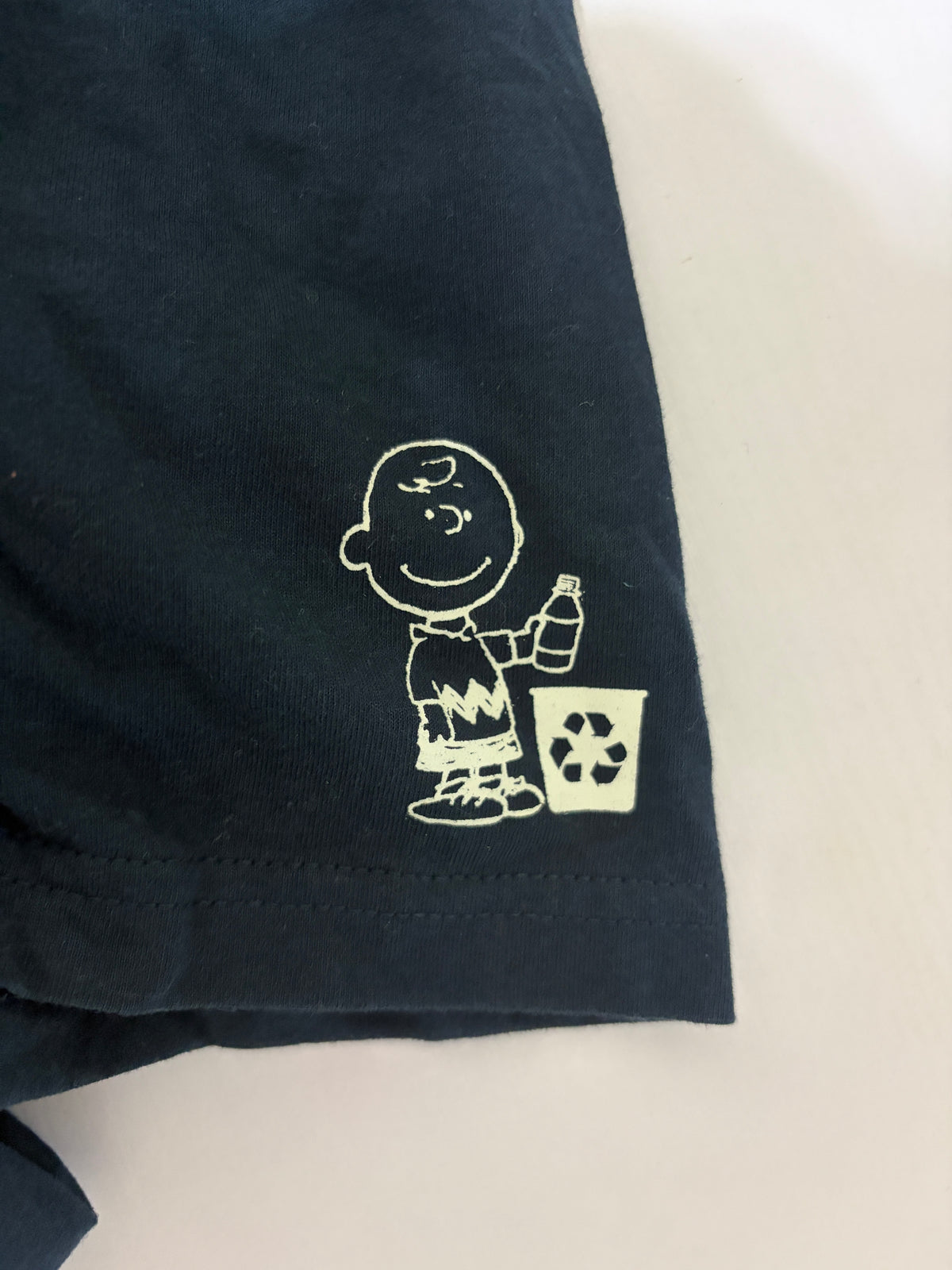 Close-up detail of the white Charlie Brown recycling graphic printed on the sleeve of a navy blue t-shirt