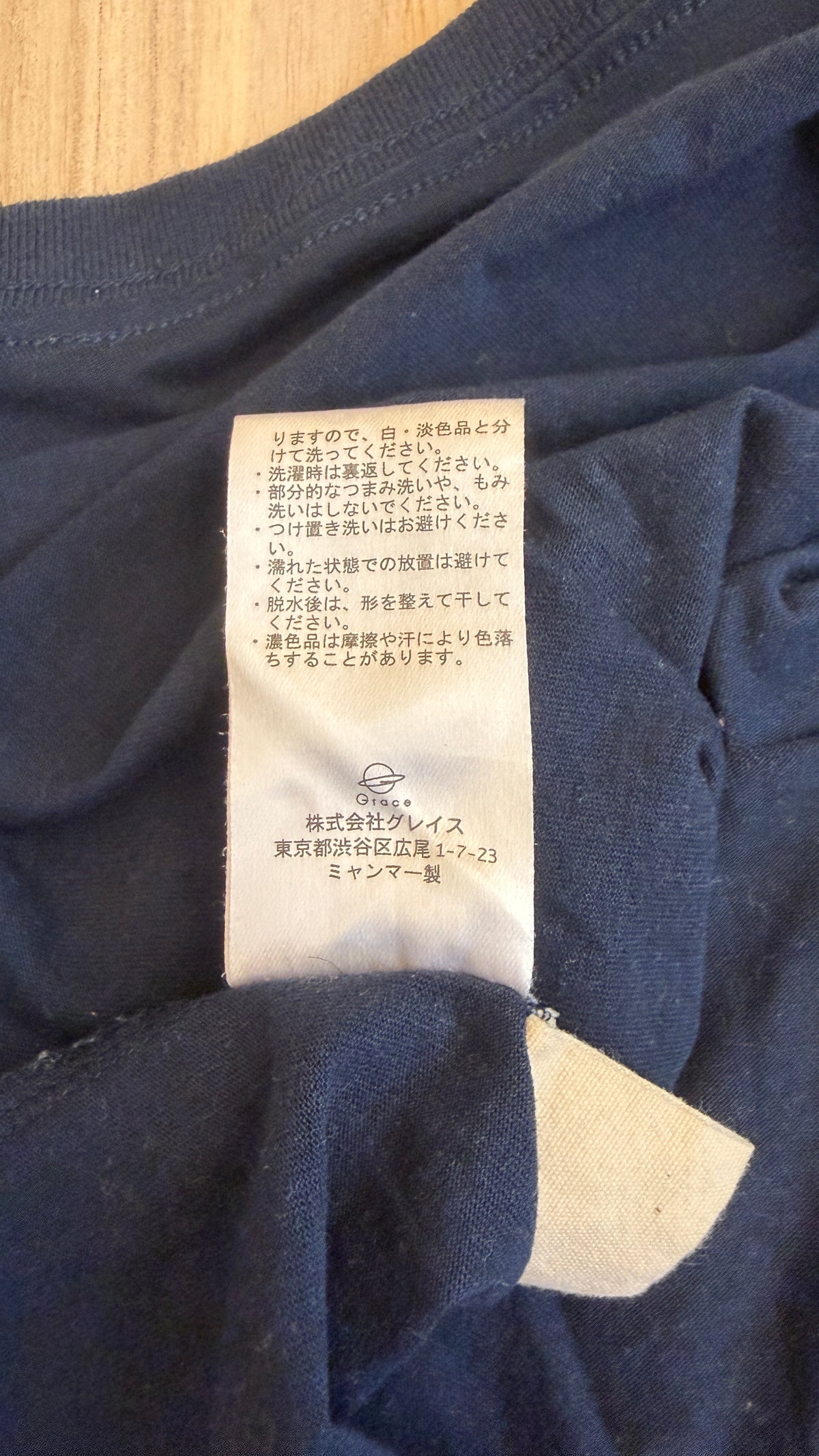 Close-up view of the white Japanese care instruction tag stitched inside a navy Peanuts Snoopy t-shirt showing washing instructions and Grace Co. manufacturer details