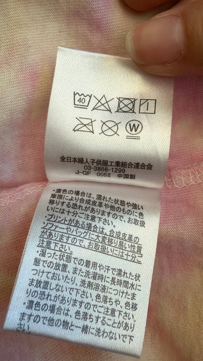 Close-up view of the inner white Japanese care instruction tag on a pastel tie-dye t-shirt displaying laundry symbols and washing warnings