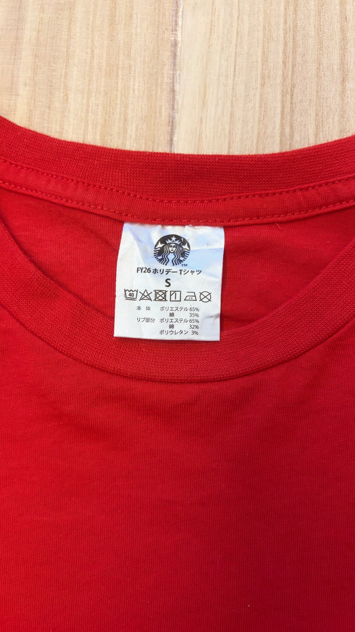 Close-up detail of the white Starbucks Siren logo inner neck label and size S care tag on a red holiday t-shirt