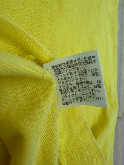 Close-up view of the reverse side of an inner white fabric care tag on a yellow t-shirt displaying Japanese text instructions for washing, drying, and ironing