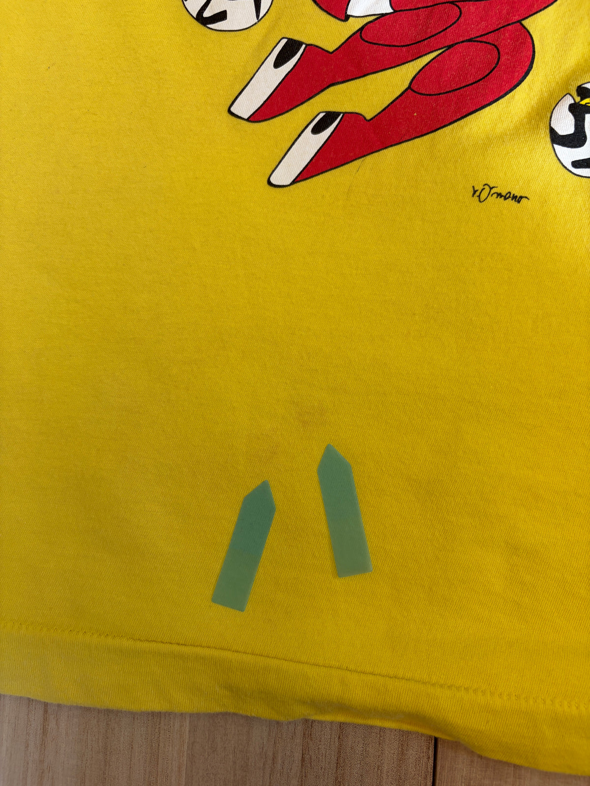 Close-up view near the bottom of a yellow Yoshitaka Amano 24 Hour Television 2014 charity t-shirt showing a light stain defect marked with green stickers.