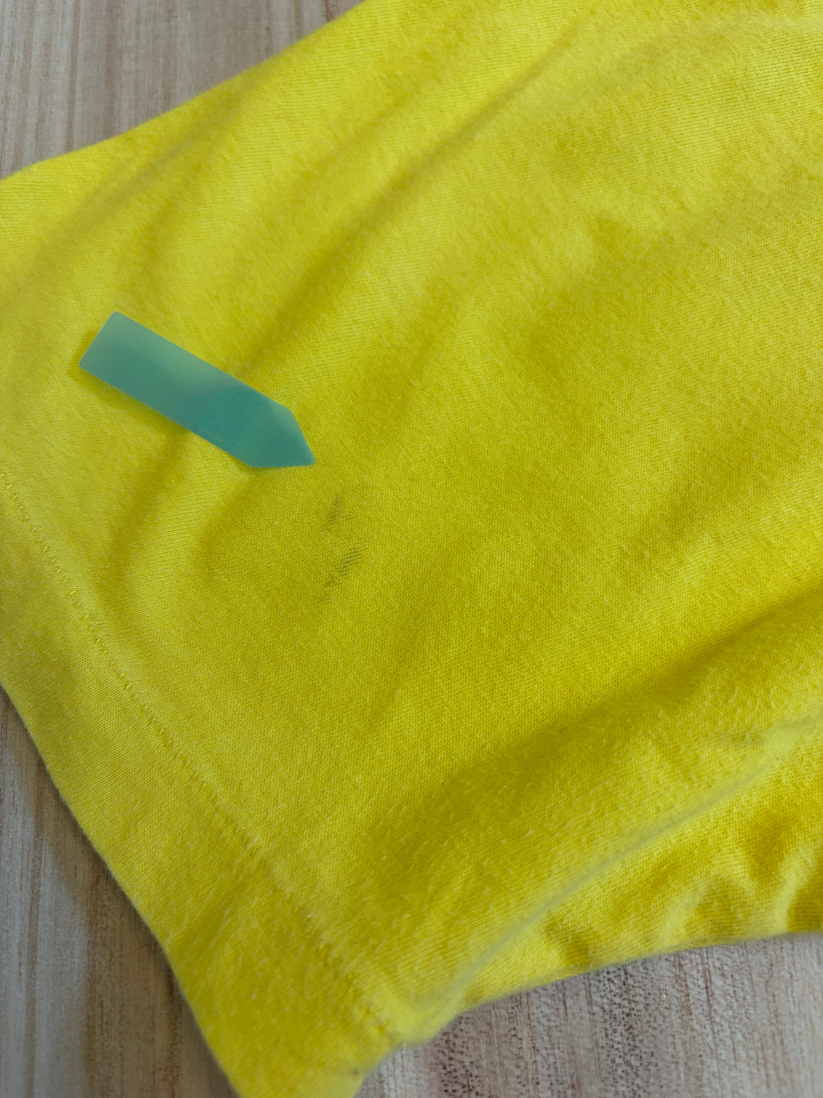 Close-up view of a yellow Yoshitaka Amano 24 Hour Television 2014 charity t-shirt showing a faint smudge stain defect pointed out by a green sticker.