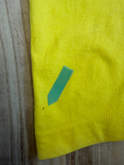 Close-up view of the bottom hem on a yellow Yoshitaka Amano 24 Hour Television 2014 charity t-shirt showing a tiny hole defect indicated by a green sticker.
