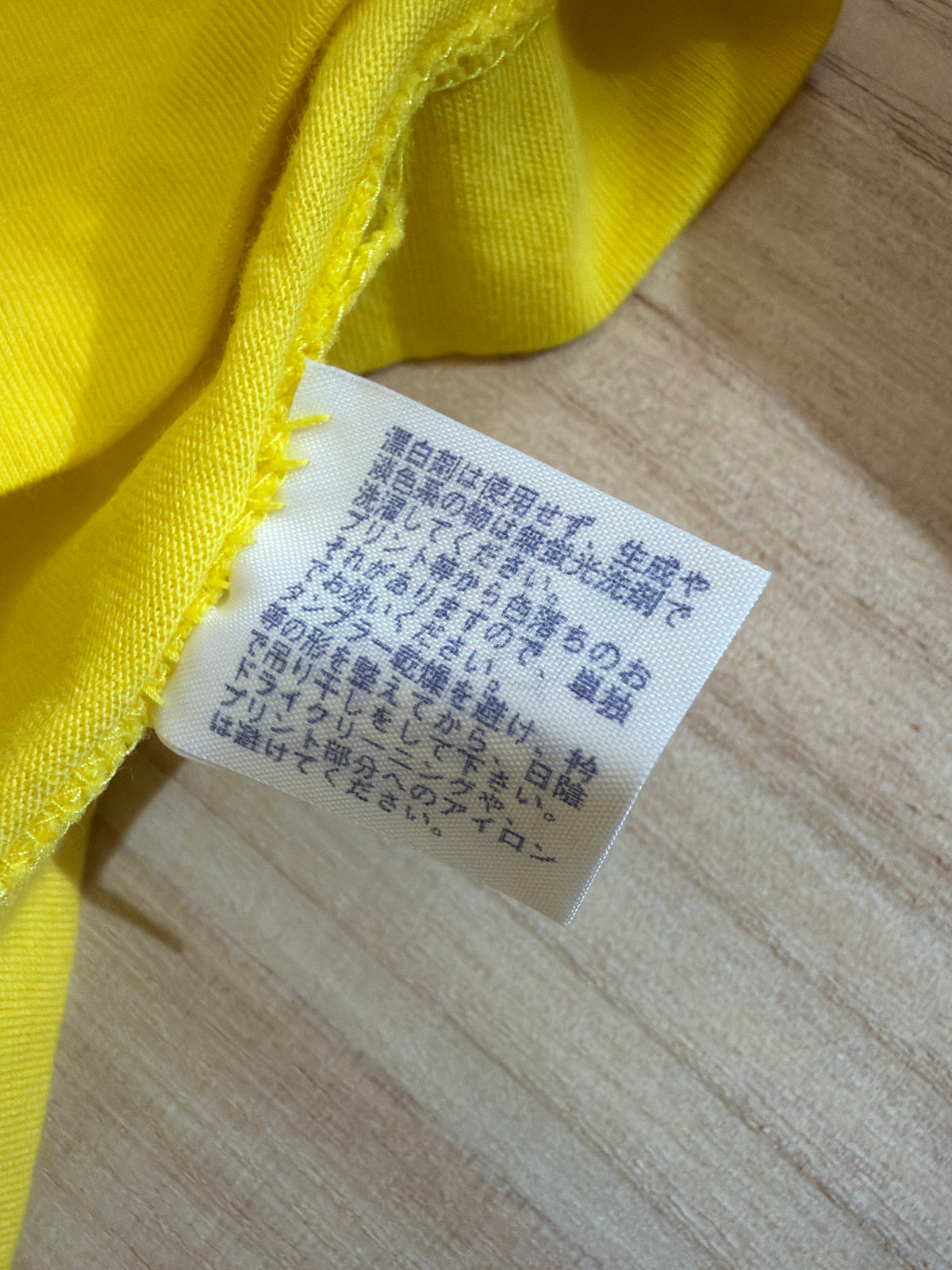 Close-up view of the reverse side of an inner white fabric care tag on a yellow t-shirt showing Japanese text instructions for washing, drying, and ironing graphic prints