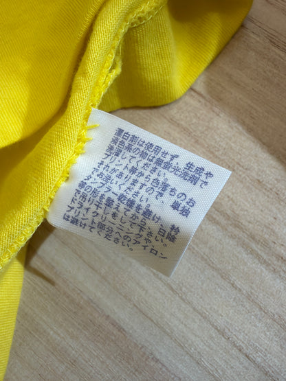 Close-up view of the reverse side of an inner white fabric care tag on a yellow t-shirt showing Japanese text instructions for washing, drying, and ironing graphic prints
